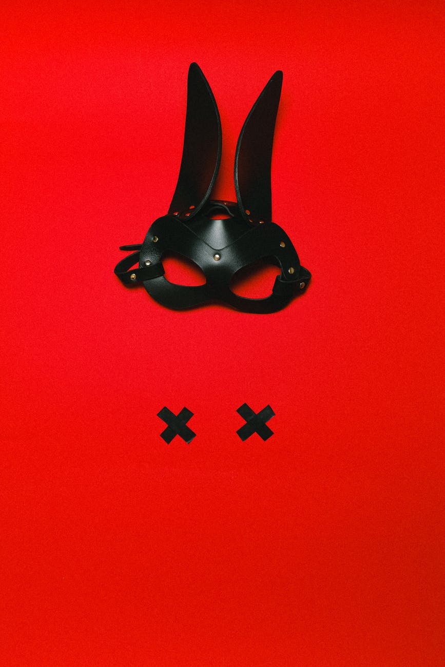 A red background with a black, leather bunny mask, and two black Xs, imitating nipples.
